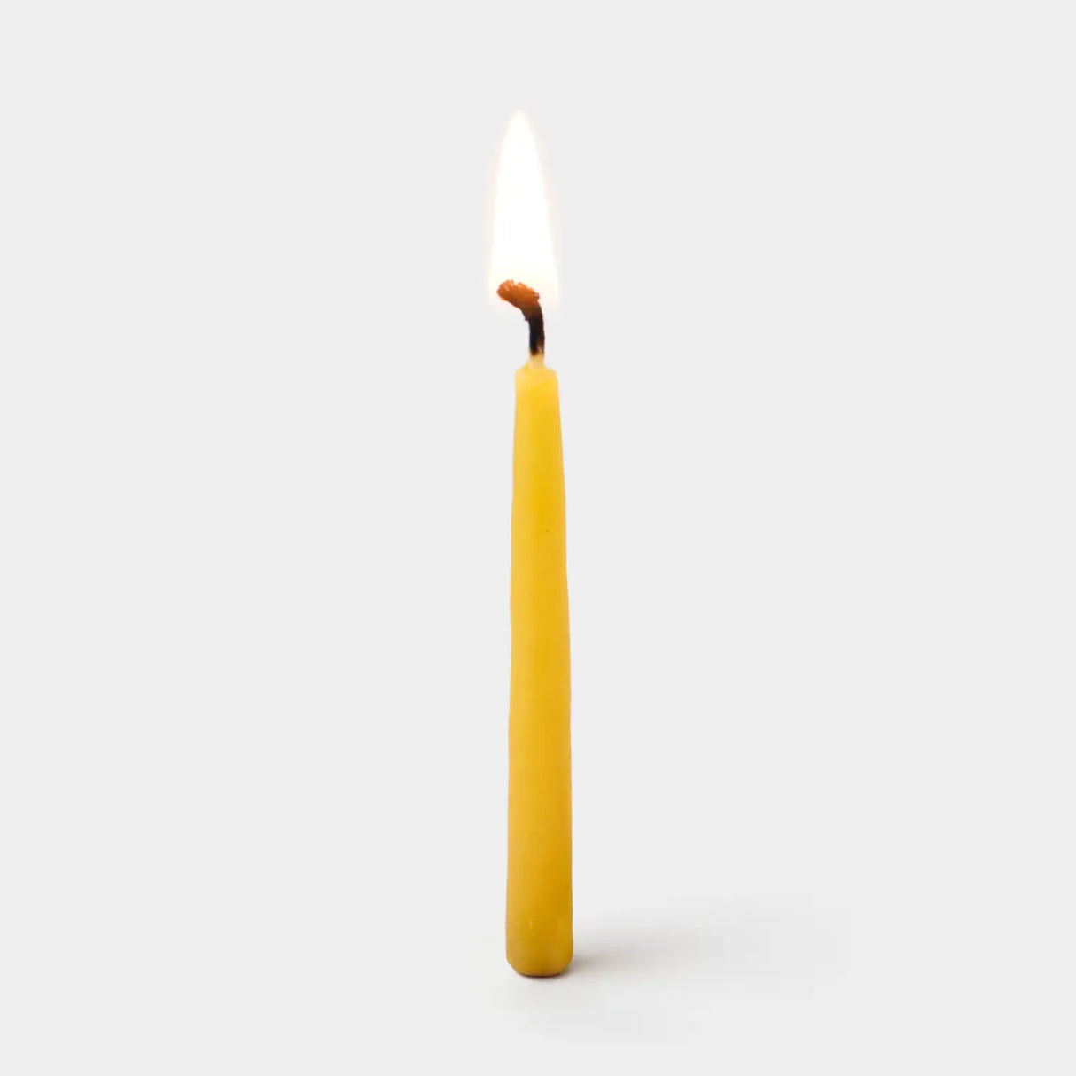 Single yellow candle with a lit wick on a white background
