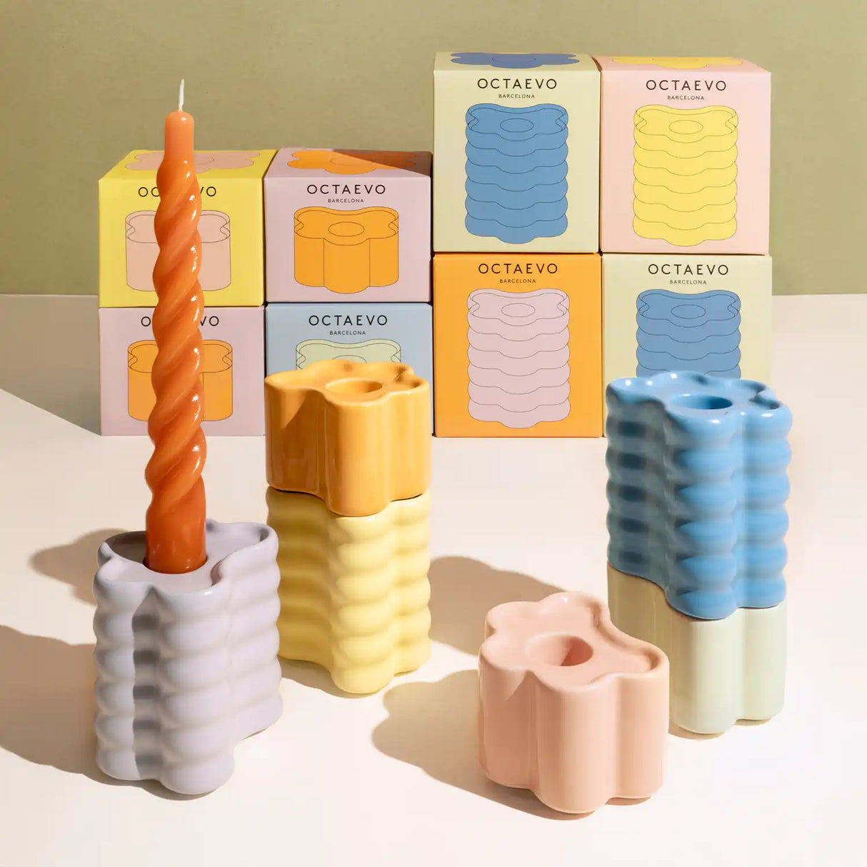Colorful candles and candle holders with Octaevo packaging on a reflective surface.