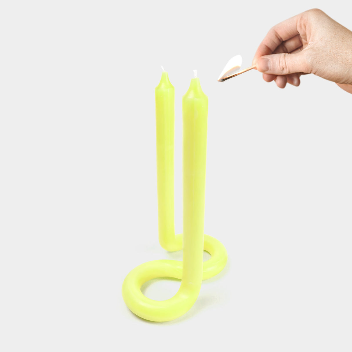 Yellow spiral candles being lit with a match on a white background