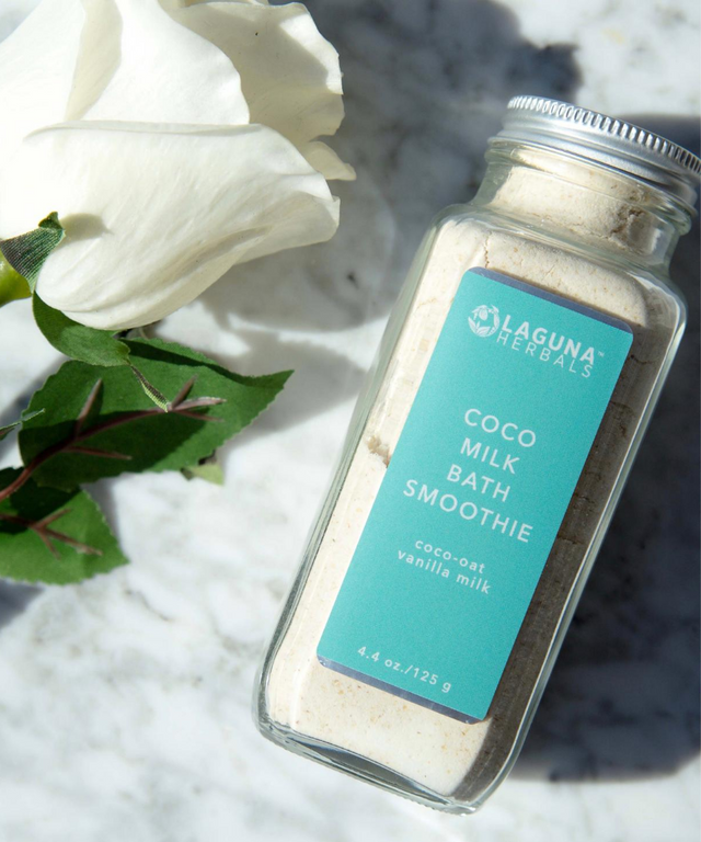 Bottle of Laguna Herbals Coco Milk Bath Smoothie with white flowers and green leaves on a marble surface