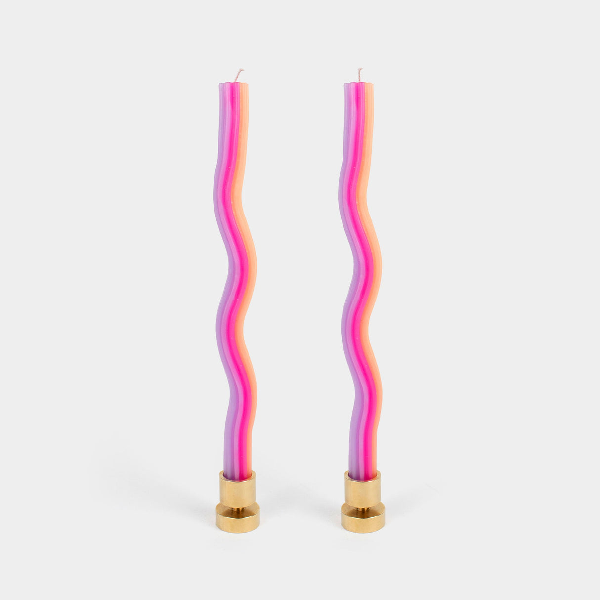 Two wavy, multicolored candles with gold bases on a light gray background