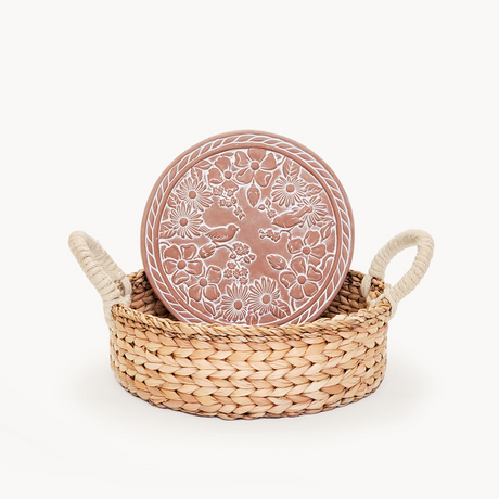 Decorative terracotta plate with floral patterns in a woven basket on a white background