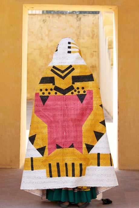 Woman wearing a colorful quilted garment with geometric patterns in a room.