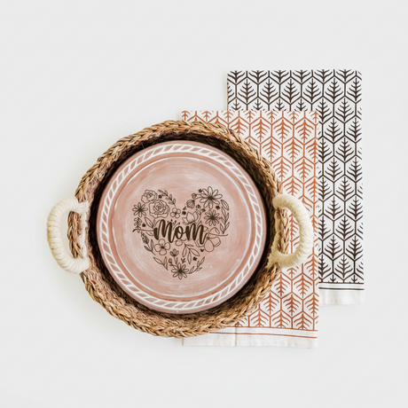 Ceramic plate with 'Mom' design in a woven basket on a white background