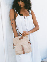 Woman holding a woven handbag with leather straps against a white background