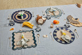 Dining setup on a striped tablecloth with place mats, cutlery, and food items.