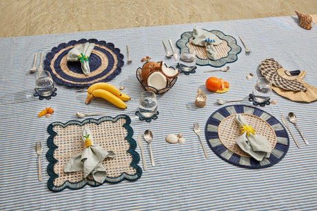 Dining setup on a striped tablecloth with place mats, cutlery, and food items.