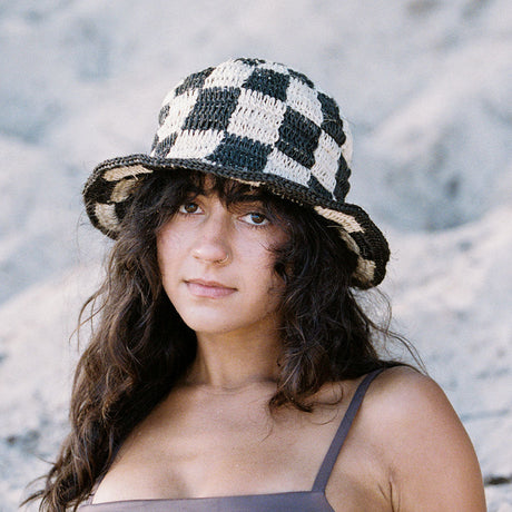 Woman wearing a checkered bucket hat against a blurred natural background
