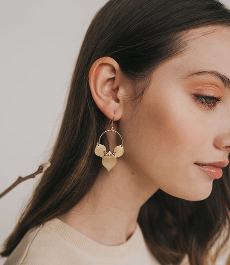 Close-up of a woman wearing gold hoop earrings with a neutral background