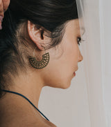 Close-up of a woman wearing a gold hoop earring with a neutral background