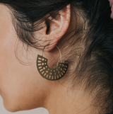 Close-up of a person wearing a gold hoop earring with a perforated design.