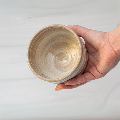 A hand holds an empty Beige Ceramic Matcha Bowl crafted in traditional Minoyaki style against a light gray background.
