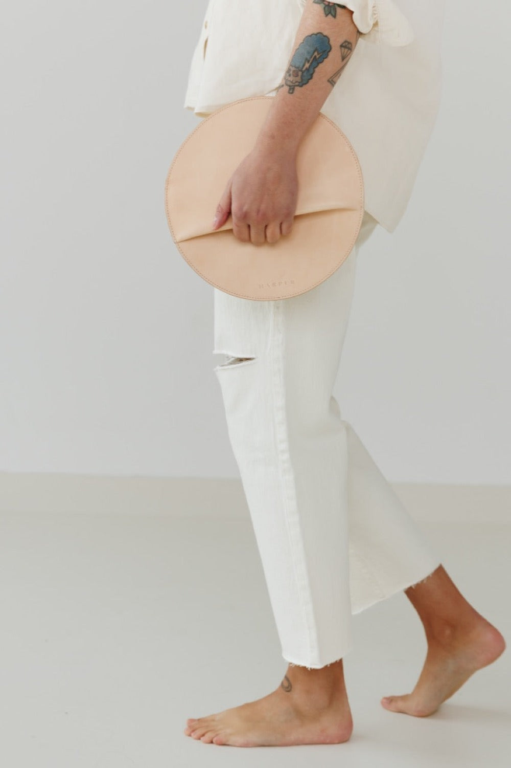Person holding a beige circular clutch against a plain background