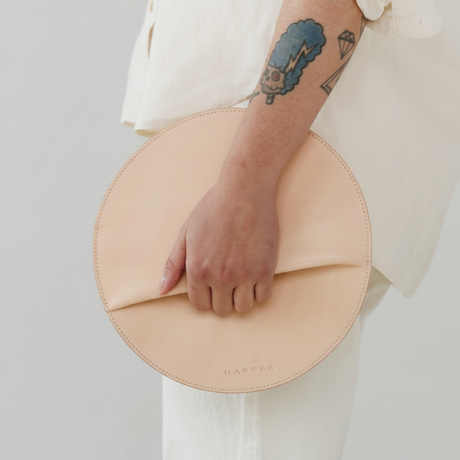 Person holding a beige circular clutch bag against a plain background