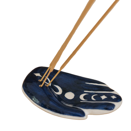 Blue ceramic dish with white patterns holding incense sticks on a wooden surface.