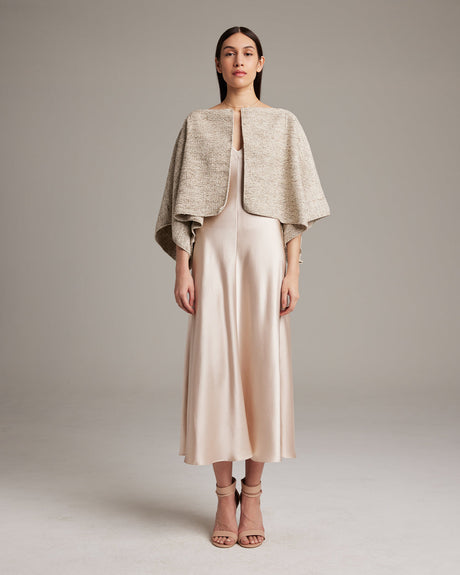 Woman wearing a beige cape over a dress on a plain background