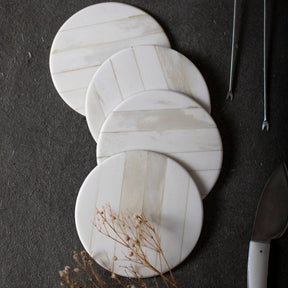 A set of four round bone-clad coasters with a stainless steel base, displayed on a dark surface.