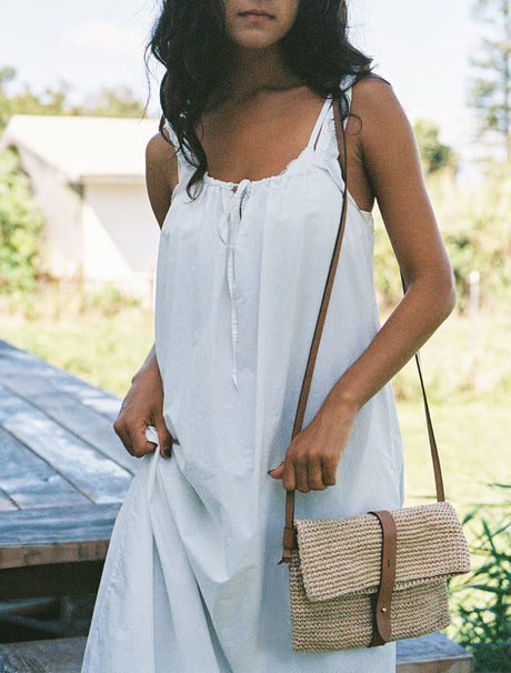 Woman in a light blue dress holding a straw bag outdoors