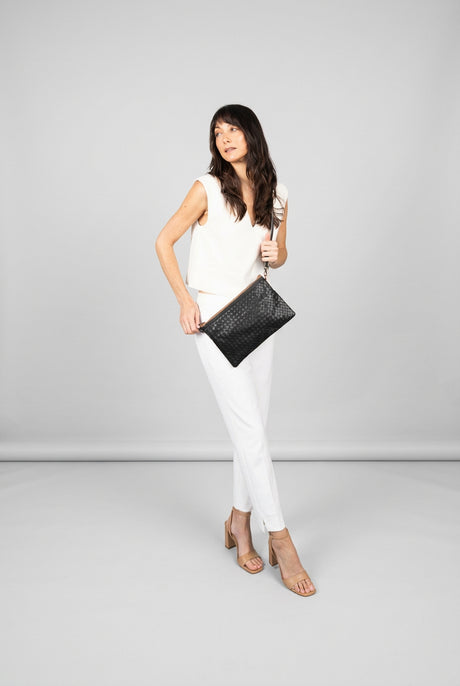 Woman holding a black clutch against a green and beige wall.
