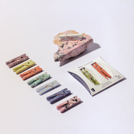Set of colorful stone clothespins on a white background with a rock and card.
