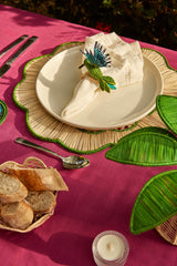 Table setting with a white plate, bread basket, and decorative napkin on a pink tablecloth.