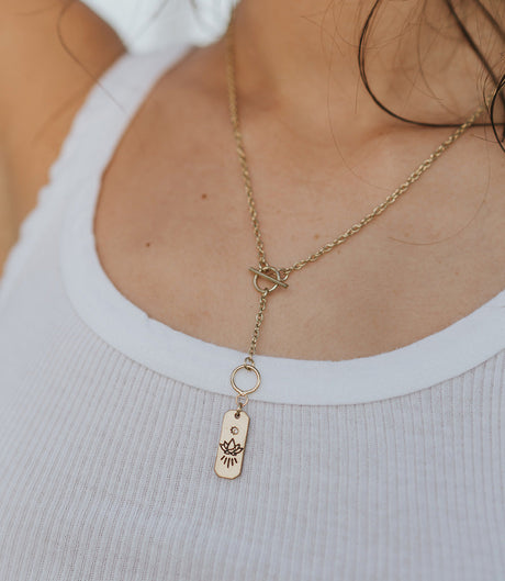 Gold necklace with a pendant worn by a person in a white tank top.
