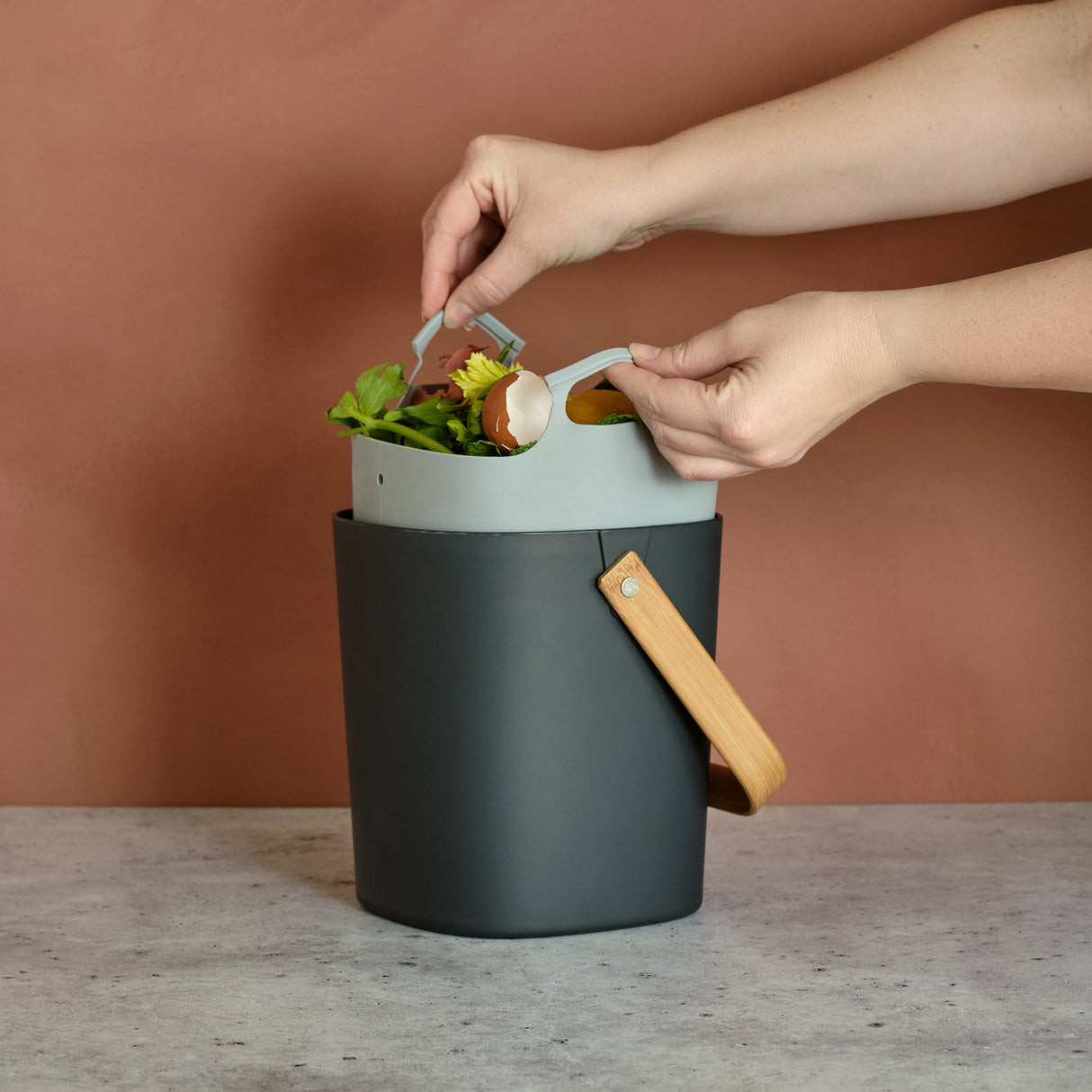 Person using a small compost bin with a brown background