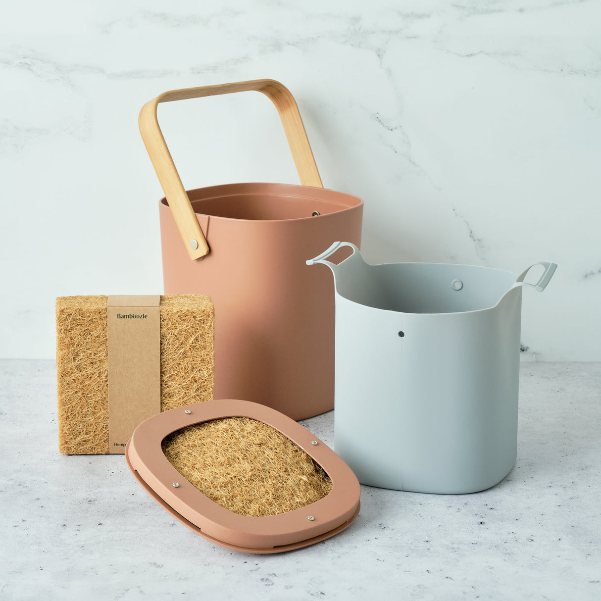 Set of gardening tools including a pink pot, gray watering can, and brown gardening tools on a light surface.