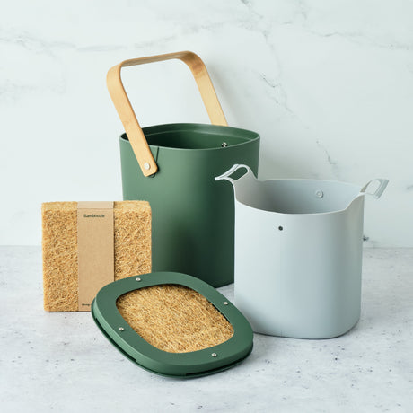 Set of gardening tools including a green bucket, white pot, and brown sponge on a light gray surface.