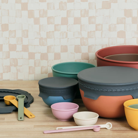 Set of colorful silicone kitchenware on a wooden surface with a checkered wall background
