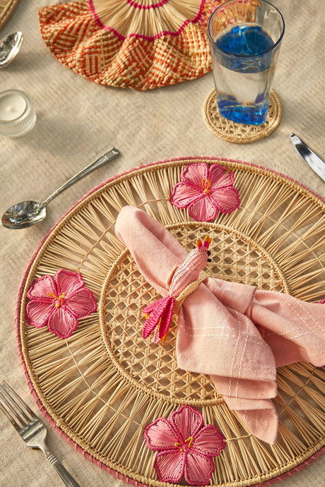 Woven placemat with pink flowers and a folded napkin on a table setting.