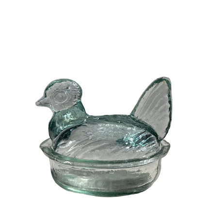 Glass duck-shaped container next to a wooden egg on a white background