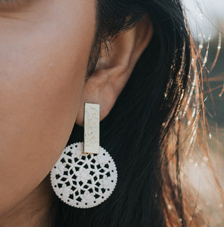 Close-up of a person wearing a white lace earring with a beige bar.