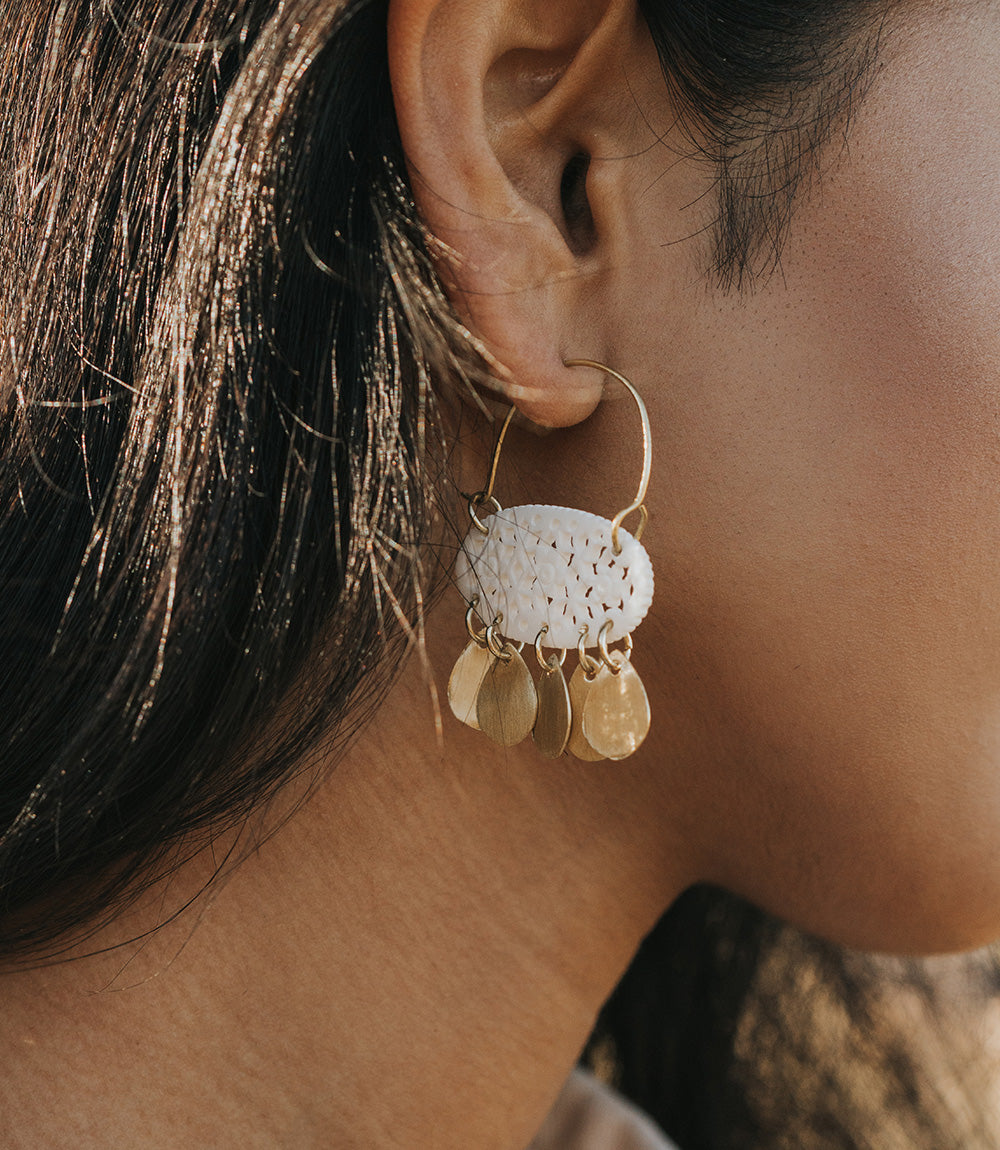 Close-up of an ear wearing a gold and white earring.