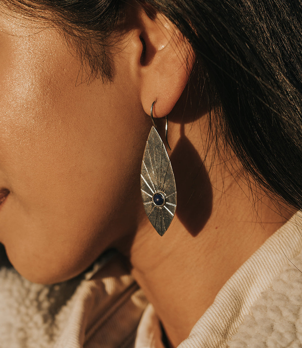 Close-up of a person wearing a silver earring with a dark gemstone.