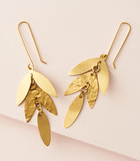 Gold leaf-shaped earrings on a light pink background