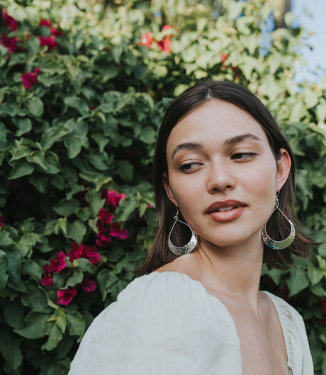 Woman with hoop earrings standing in front of green foliage and flowers