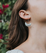 Close-up of a person wearing a silver hoop earring with a textured pattern, outdoors.