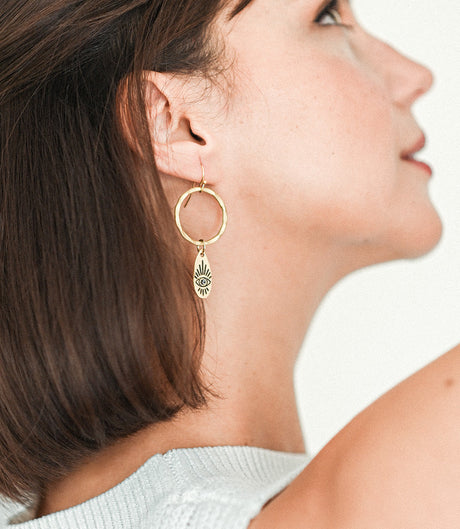 Close-up of a woman wearing a gold hoop earring with a small pendant.