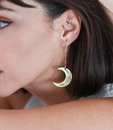 Close-up of a woman wearing a gold crescent moon earring with intricate designs.