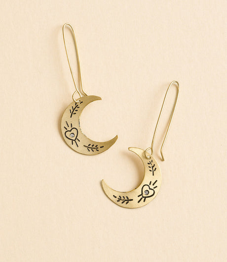 Gold moon-shaped earrings with heart and leaf designs on a beige background