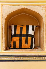 Decorative pillow with black, white, and orange pattern in an ornate archway.