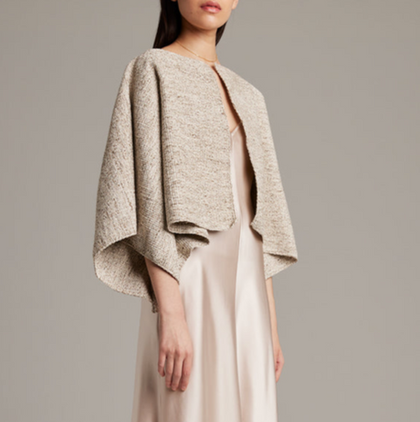 Woman wearing a beige textured jacket over a plain dress on a neutral background