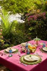 Outdoor dining table setting with pink tablecloth, greenery, and tropical plants.