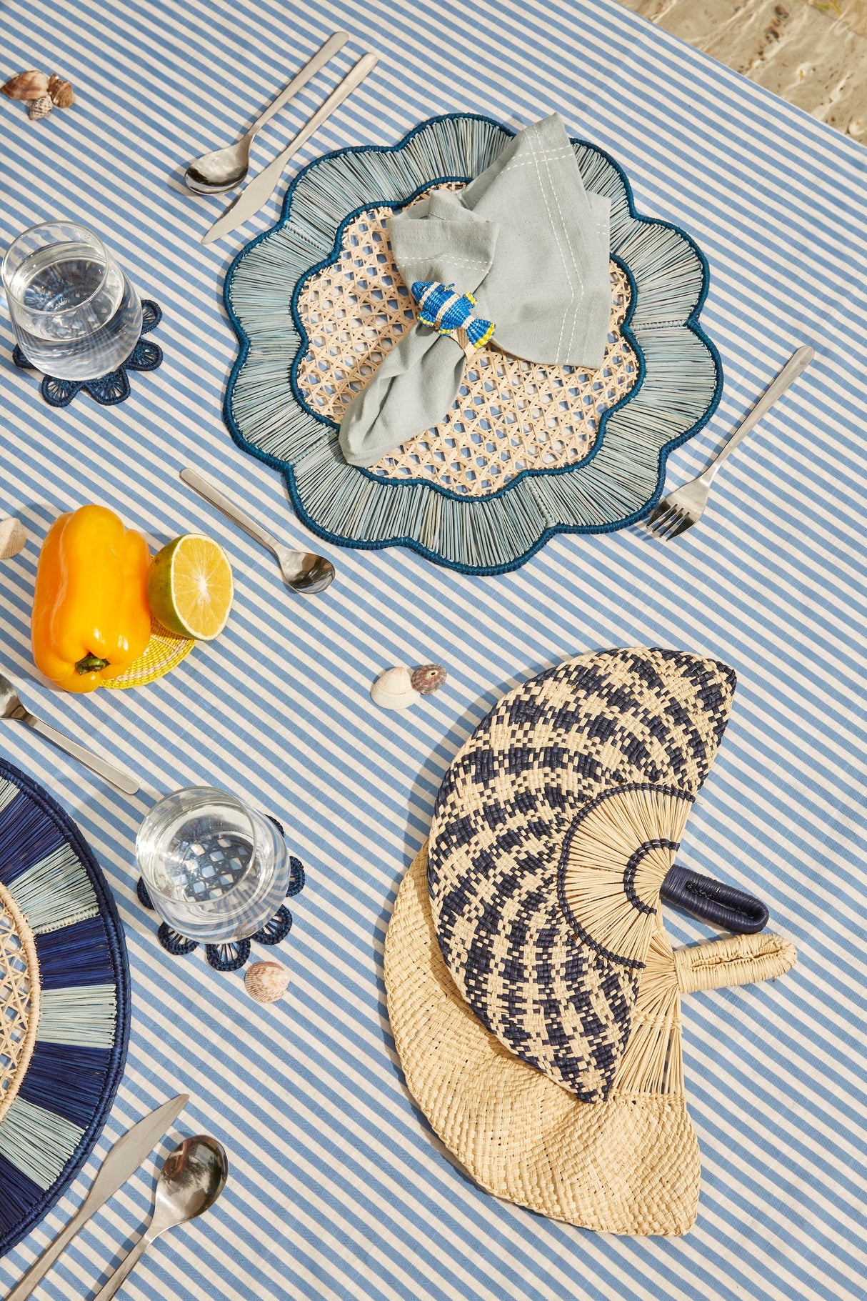Table setting with woven placemats, cutlery, and glasses on a striped tablecloth.