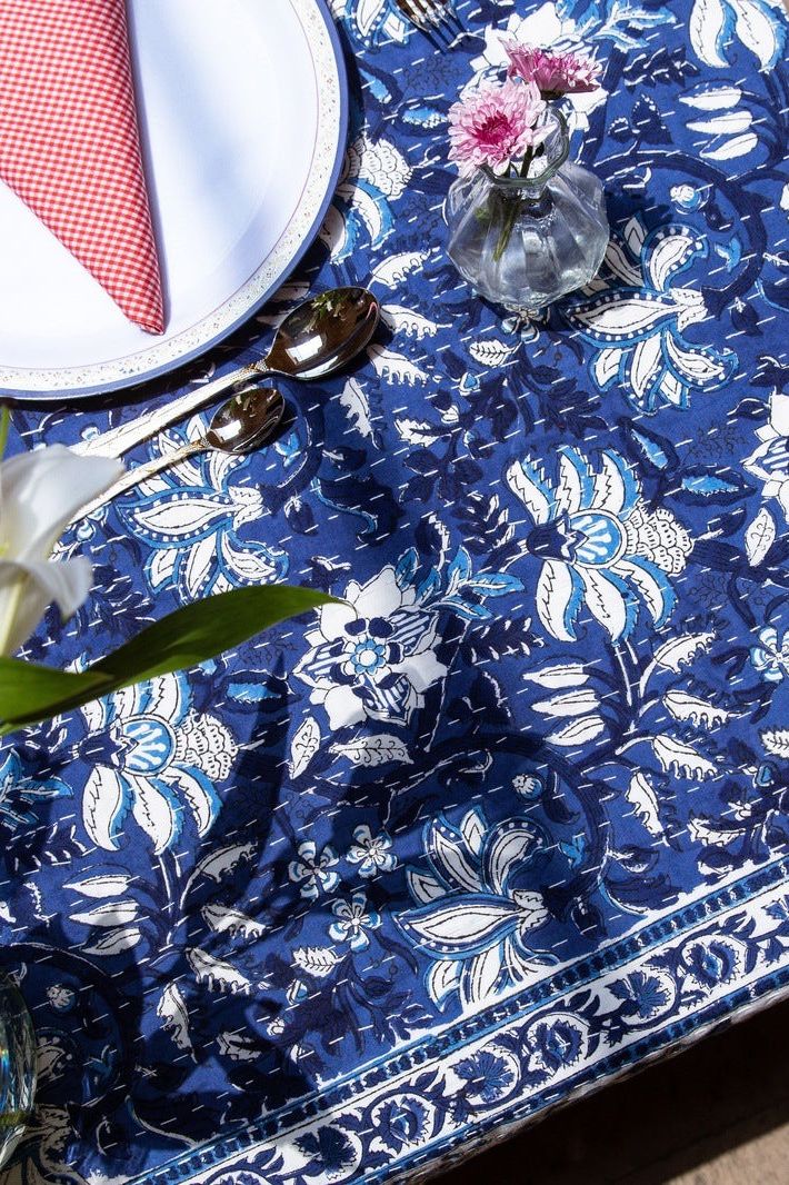 Blue floral tablecloth with a white plate, red napkin, and silverware on a table.