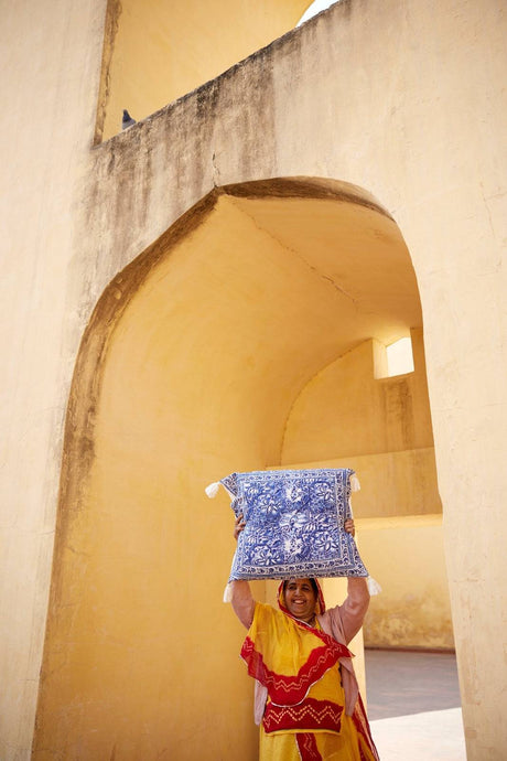 Woman holding a blue and white patterned pillow in front of a yellow archway.