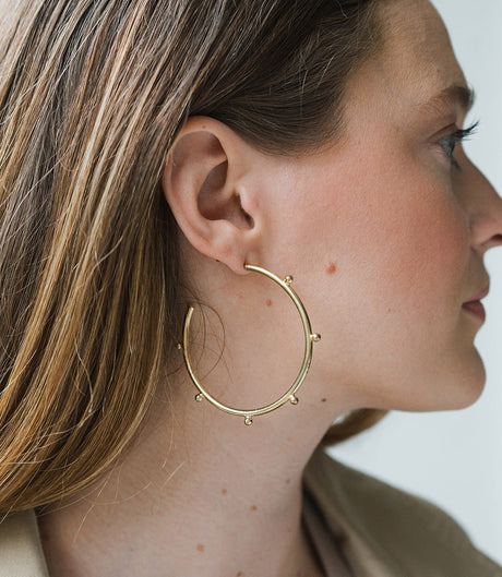 Close-up of a person wearing a gold hoop earring with a neutral background
