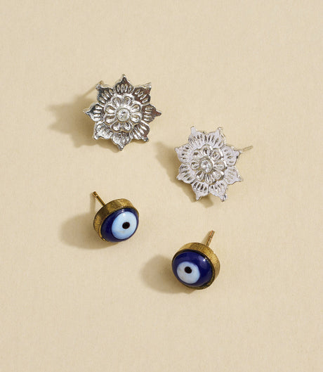 Set of silver floral earrings and gold evil eye earrings on a beige background