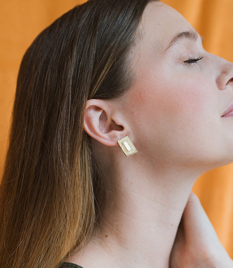 Woman wearing gold earrings against an orange background
